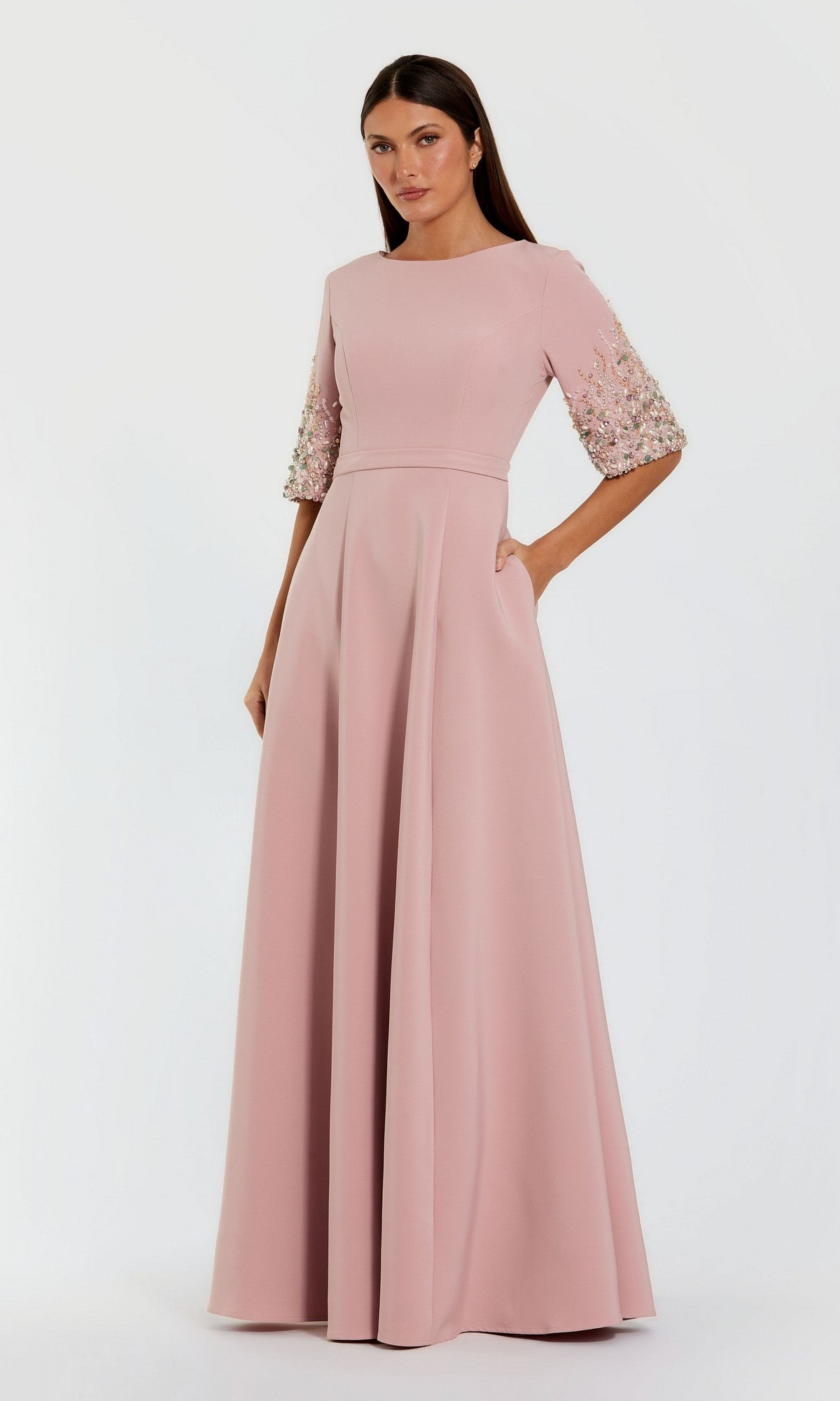 Woman in a Mac Duggal 2322 Long Formal Dress in rose, featuring a floor-length crepe design with a fitted bodice and floral-embellished three-quarter sleeves, standing against a plain white background.